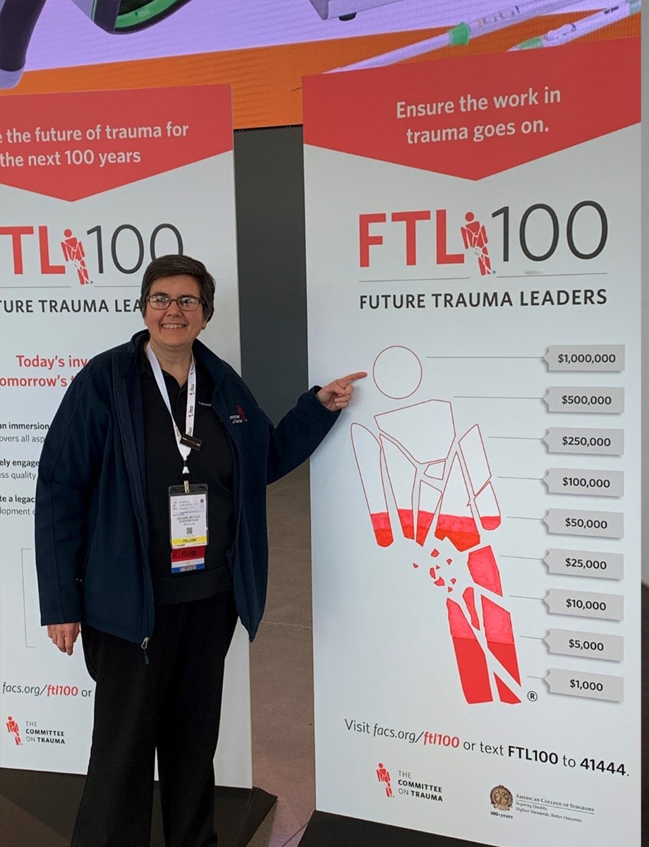 Dr Bulger stands against a donation chart showing the goal for the FTL100 campaign. 